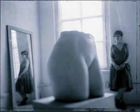 Photograph of an exhibition space with a rounded object, framed work and a standing figure